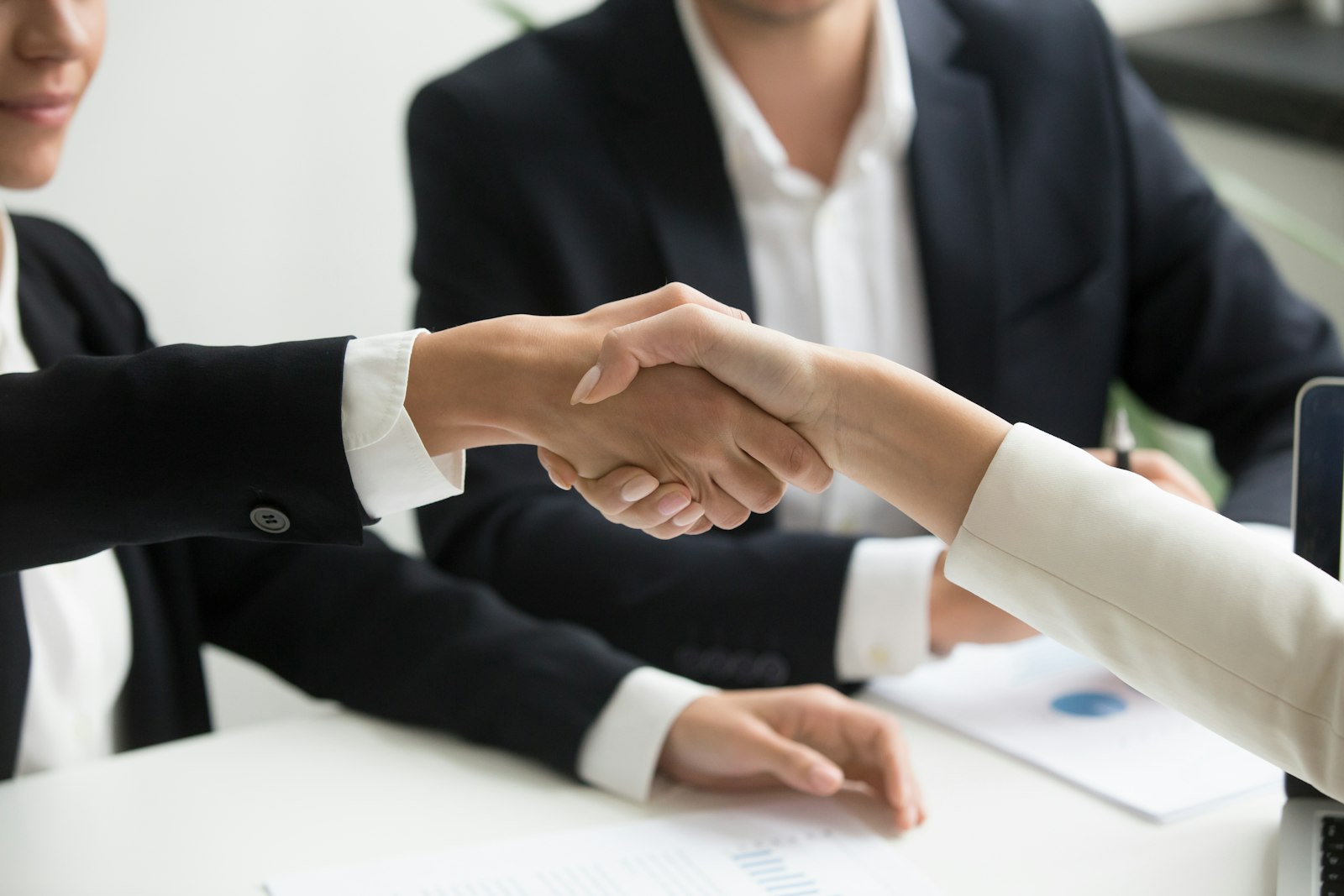 Dos personas se dan la mano frente a una laptop, símbolo de la integración entre marketing y ventas con un CRM